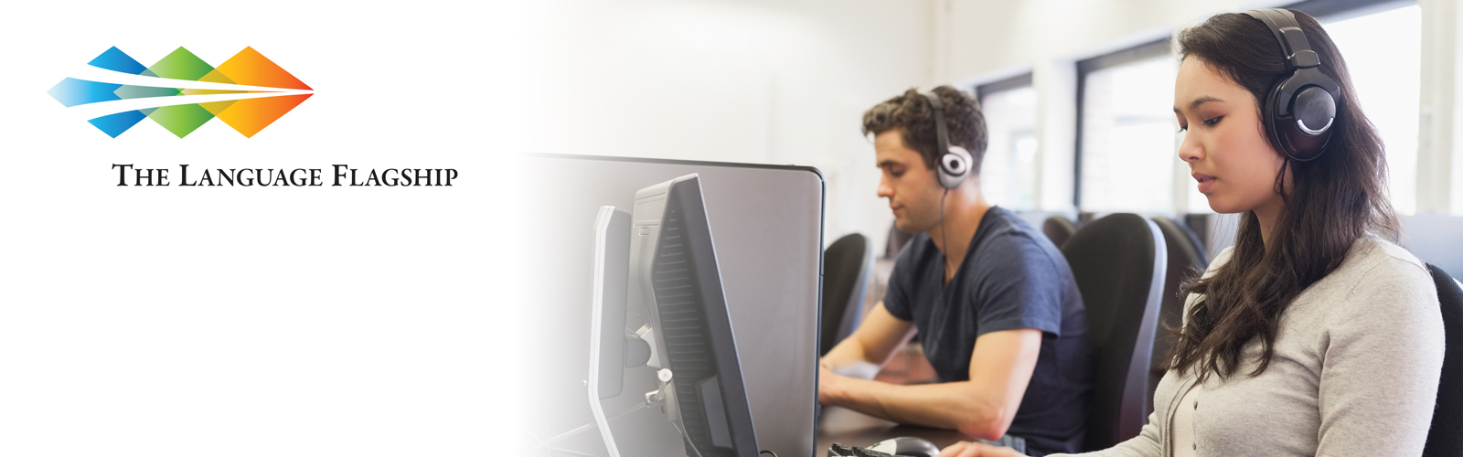 Students wearing headphones and sitting at computers while taking online proficiency assessments.